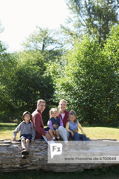 Portrait of a family of five sitting on a log.