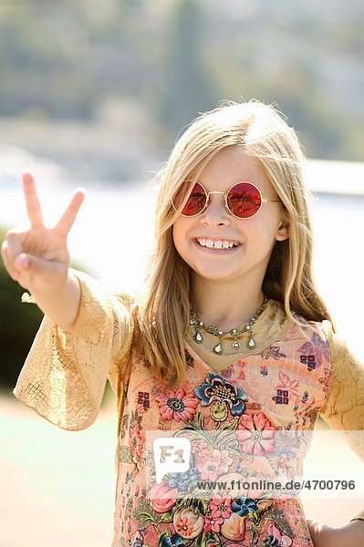 Young girl in sunglasses making a peace sign.
