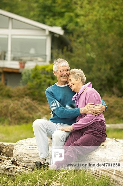 Senior couple sitting together on a log at the beach.