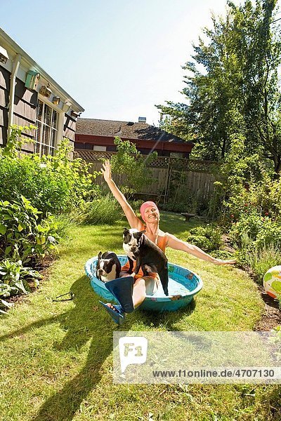 Woman sitting in a wading pool with two dogs