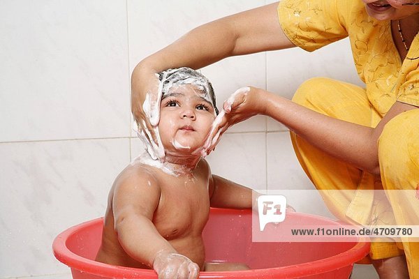 Mother giving bath to one and half year old baby applying soap to her face R 687A and 687B