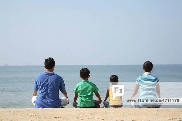 South Asian Indian parent and children facing Arabian Sea sitting on seashore  Shiroda   Dist Sindhudurga  Maharashtra  India MR 703D  703E 703F 703G