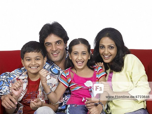 South Asian Indian family with father mother son and daughter sitting on sofa enjoying and looking at camera MR 698 699 700 701