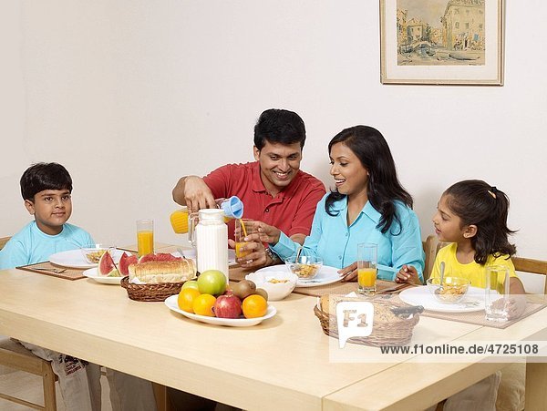 Father pouring juice in glass with family sitting on dining table for breakfast MR702R MR702S MR702T MR702U