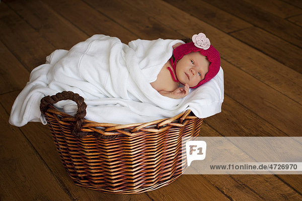 Newborn baby girl  two weeks old  with little red cap  lying in a basket