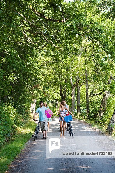 Vier junge Menschen mit Fahrrädern zu Fuß auf ländliche Straße
