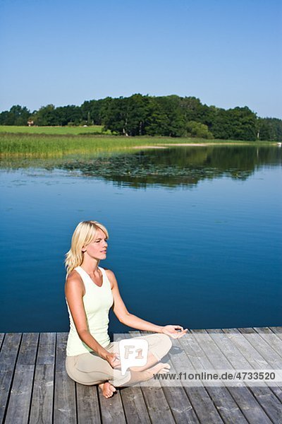 Young woman meditating on jetty