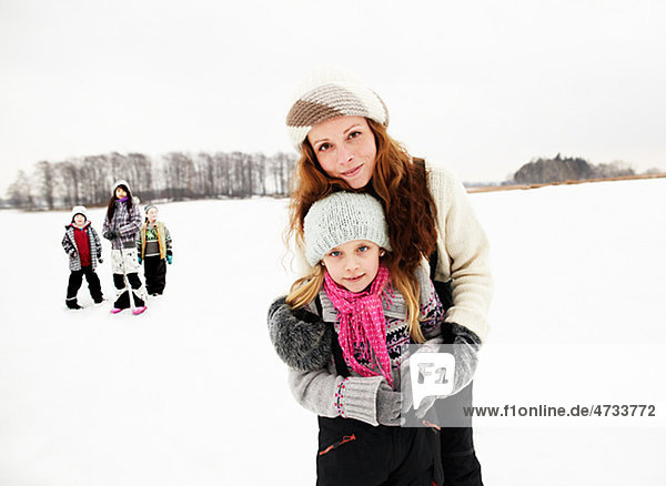 Portrait of mother embracing daughter in snow  friends in background