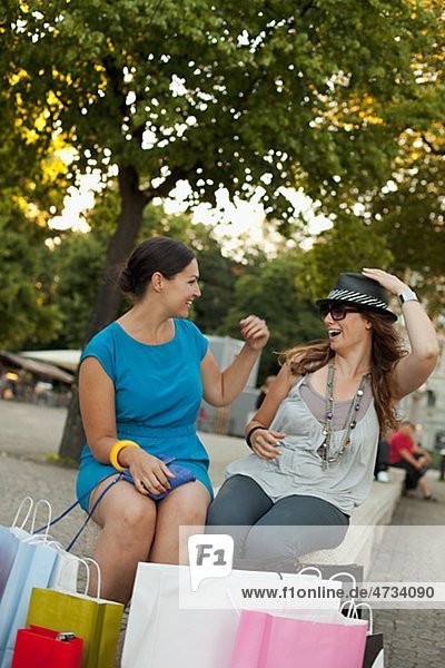 Two women sitting on bench with shopping bags  laughing