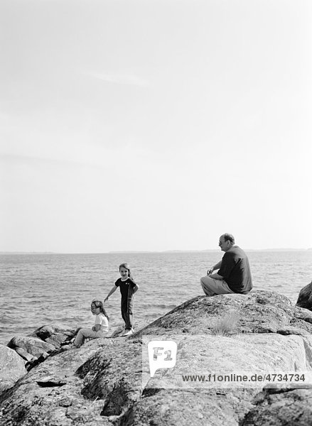 Mädchen und älterer Mann auf Felsen mit Meer im Hintergrund