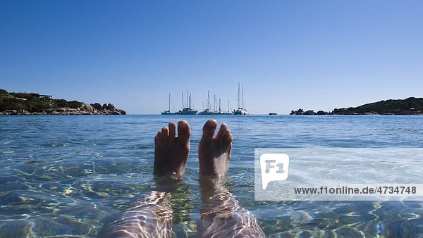 Füße im Wasser mit Yachten am Horizont