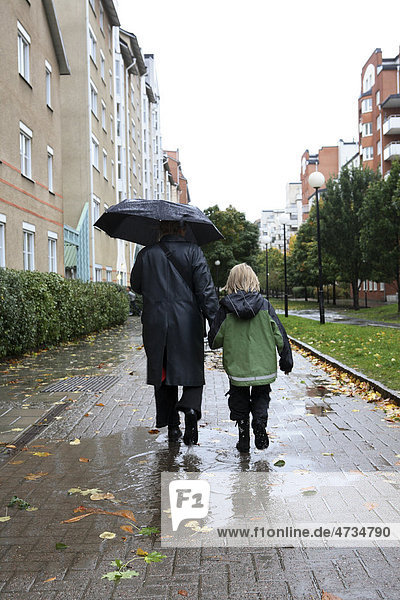 Mutter und Sohn Spaziergang durch Bürgersteig während der Regen