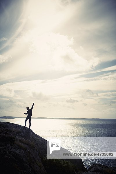 Silhouette of man celebrating on cliff by sea