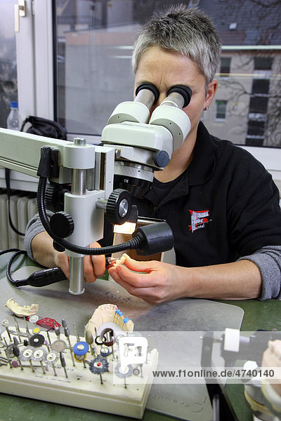 Dental laboratory  manufacture of a dental prosthesis by a master craftsman  working on a dental bridge under a stereo microscope