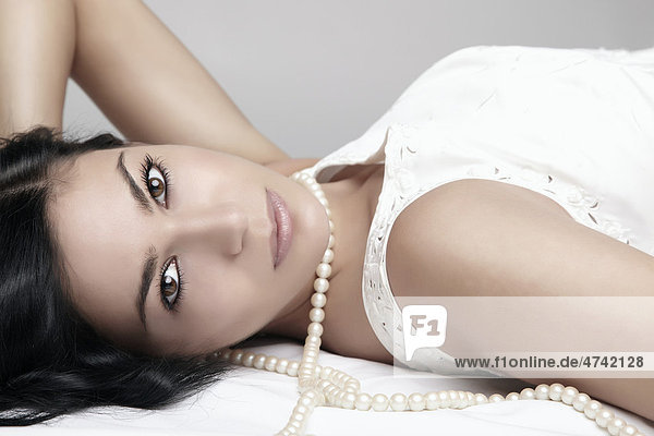 Portrait einer auf dem Boden liegenden Frau in weißem Kleid und Perlenkette