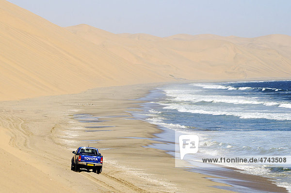 Geländewagen fährt am Strand des Atlantischer Ozean Richtung Sandwich Harbour  Namib Naukluft Nationalpark  Teil des Namib-Skelettküste Nationalparks  Skeleton Coast  Wüste Namib  Namibia  Afrika