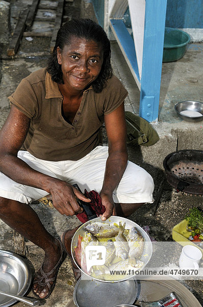 Frau kocht ein Fischgericht vor ihrem Haus in einem Armenviertel von Petit Goave  Haiti  Karibik  Zentralamerika