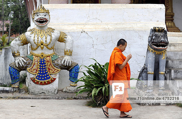 Young monk and temple guard statues  Wat Aham temple  Luang Prabang  Laos  Southeast Asia  Asia