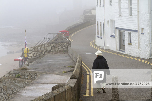 Eine Frau geht im Nebel auf einer Küstenstraße in Porthleven  Cornwall  England  Großbritannien  Europa