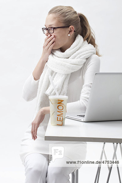 Blonde  weißgekleidete junge Frau neben einem Laptop