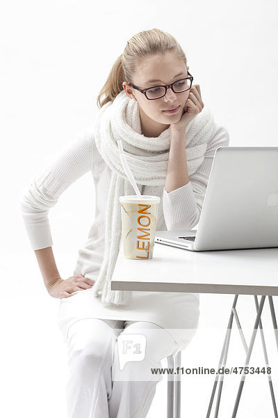 Blonde  weißgekleidete junge Frau arbeitet am Laptop