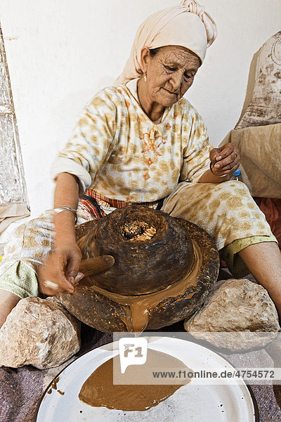 Für die traditionelle Herstellung von Arganöl mahlt eine Frau bei Essaouira geröstete Argan-Mandeln zwischen zwei Mahlsteinen  Marokko  Afrika