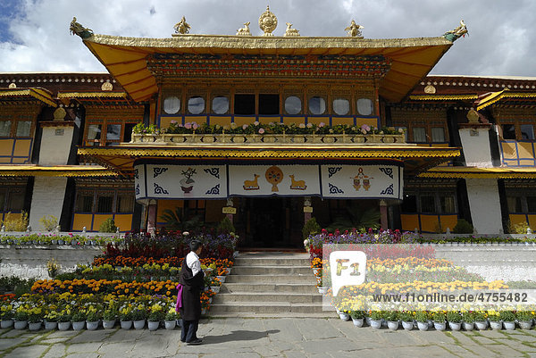 Tibetan man wearing traditional costume standing in front of the Summer Palace of the Dalai Llama in Norbulingka  meaning literally The Jewelled Park  with flowers  Lhasa  Tibet  China  Asia