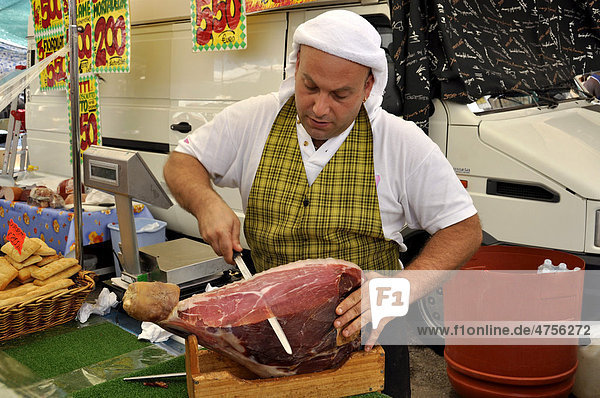 Verkäufer mit italienischem Schinken oder Prosciuto  an Spezialitätenstand auf dem Wochenmarkt  Rom  Latium  Italien  Europa