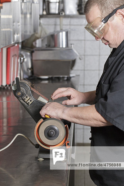 Koch schleift Messer auf Bandschleifmaschine in Küche