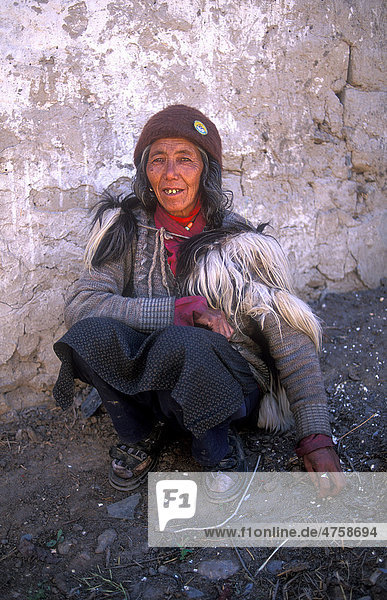 Eine ältere Frau in traditioneller Kleidung  mit einem Ziegenfell über den Schultern  hockt am Boden vor ihrem Wohnhaus  Zanskar  Ladakh  Himalaya  Nordindien  Indien  Asien