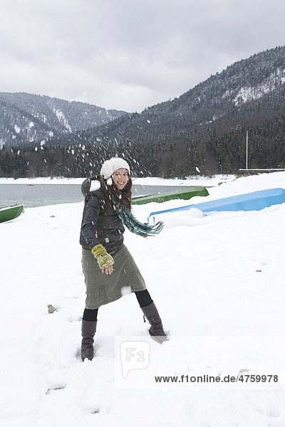 Cheerful young woman on the lakeshore of Walchensee or Lake Walchen throwing a snowball  winter  Bavaria  Germany  Europe