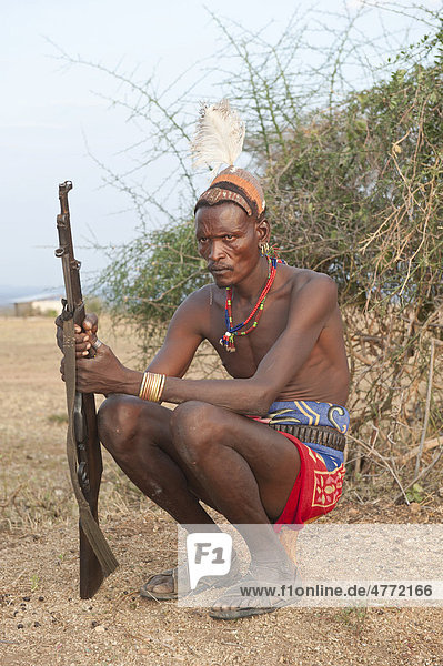 Hamar Krieger mit typischer Lehm Haarfrisur und Feder  mit Gewehr  sitzt auf seiner Kopfstütze  Omo-Tal  Süd Äthiopien  Afrika