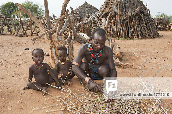 Hamar Mann mit zwei kleinen Kindern schneidet Fleisch im Dorf  Omo-Tal  Süd Äthiopien  Afrika