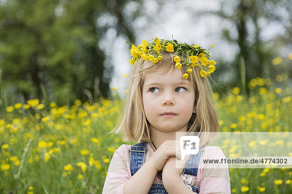 Mädchen mit einem Blumenkranz auf dem Kopf  verschränkten Händen und einem fragenden Blick  Porträt