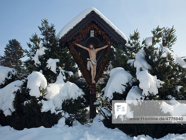 Schneebedecktes Kreuz  Kruzifix  im Gebüsch