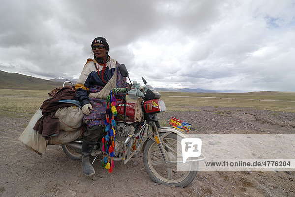 Tibetan pilgrim wearing sunglasses while sitting on a decorated and packed motorcycle on the way to Mount Kailash  in the high altitude plateau of Changtang near the Lungkar Mountains  Western Tibet  Ngari Province  Tibet  China  Asia