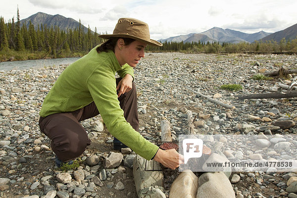 Junge Frau kocht auf einem Lagerfeuer grillt Hamburger Kiesbank Wind River Yukon Territory Kanada