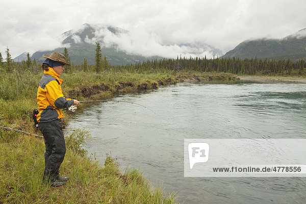 Young woman fishing  Wind River  Mackenzie Mountains behind  Yukon Territory  Canada