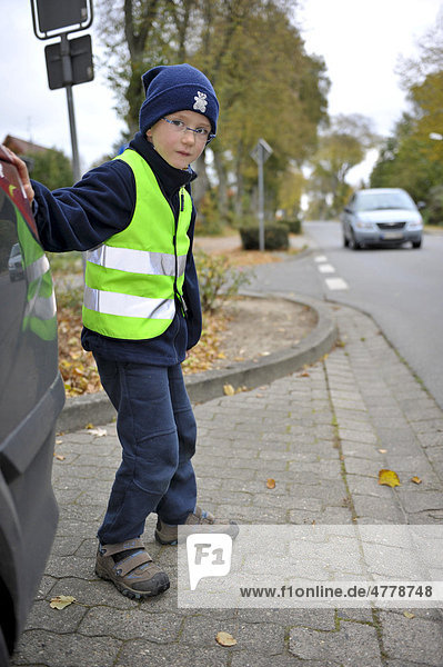 Little boy with reflective luminous vest is going to cross road
