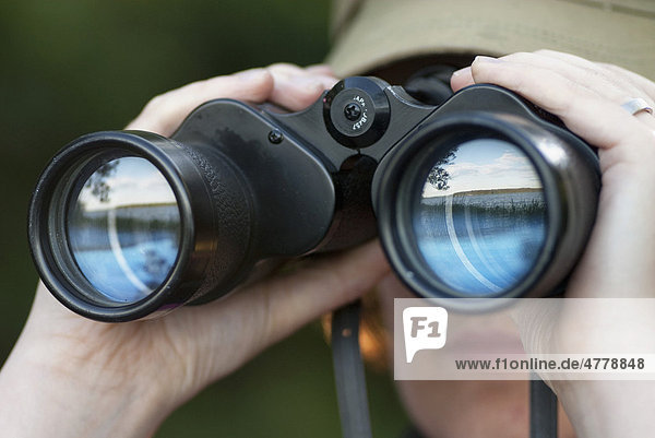 Woman looking through binoculars with reflection of a lake in the glasses