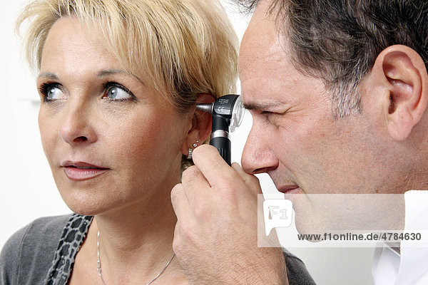 Arztpraxis  Arzt untersucht mit Hilfe einer beleuchteten Speziallupe den Gehörgang einer Patientin