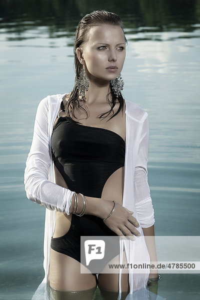 Junge Frau in einem schwarzen Badeanzug und weißem Oberteil und mit nassen Haaren beim Baden in einem See