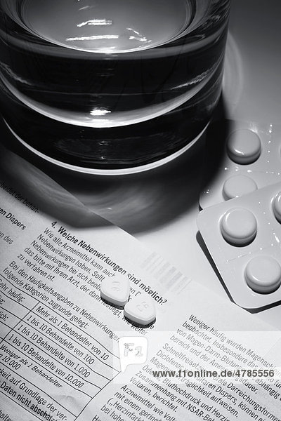 Tabletten liegen auf einem Arznei-Beipackzettel mit den entsprechenden Nebenwirkungen vor einem Wasserglas