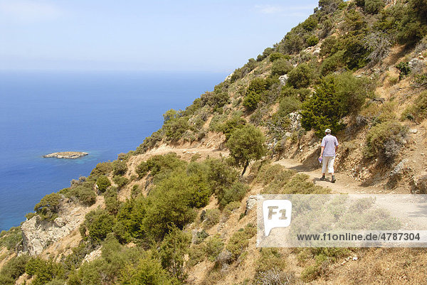 Woman hiking along a steep coastal cliff trail  looking over an island and the blue sea  descending from Moutti tis Sotiras mountain  Baths of Aphrodite  Akamas  Southern Cyprus  Republic of Cyprus  Mediterranean Sea  Europe