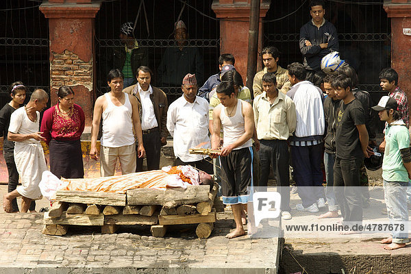 Teilnehmer eines traditionellen Begräbnis umstehen zur Verbrennung aufgebahrte Leiche eines Verwandten  während Scheiterhaufen angezündet wird  Pashupatinath  Nepal  Asien
