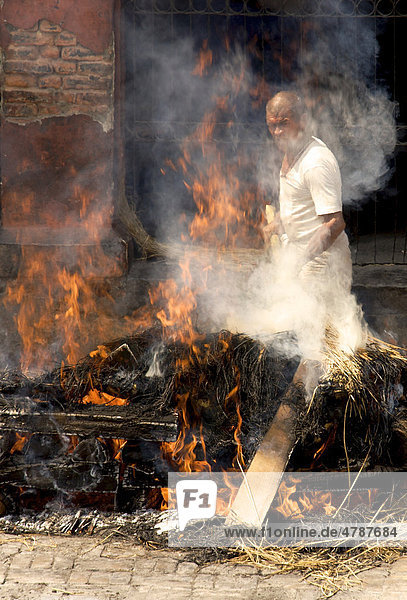 Unberührbarer Priester aus der untersten Kaste hält rauchenden Scheiterhaufen bei traditioneller Leichenverbrennung am Brennen  Pashupatinath  Nepal  Asien