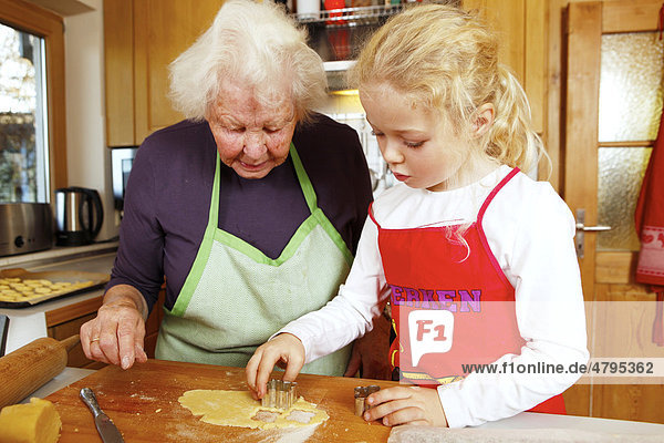 Weihnachtsbäckerei  Oma und Enkelin backen Weihnachtsplätzchen  Mädchen sticht mit Ausstechform den Teig aus