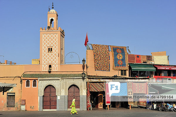 Moschee mit Minarett  daneben verkauft ein Teppichhändler seine Teppiche  Djemaa el Fna  Platz der Gehängten  Marrakesch  Marokko  Afrika