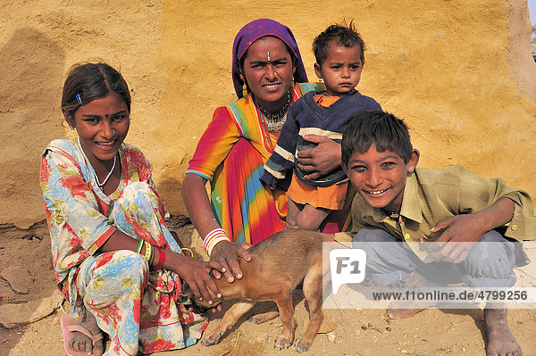 Eine Inderin hockt mit drei Kindern am Boden  gemeinsam halten sie einen kleinen Hund fest  Wüste Thar  Rajasthan  Indien  Asien