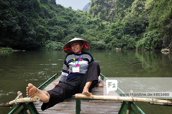 Frau rudert mit Füßen, Umgebung von Ninh Binh, unterwegs am Fluss zu den Höhlen von Trung Anh, trockene Halong Bucht, Vietnam, Südostasien